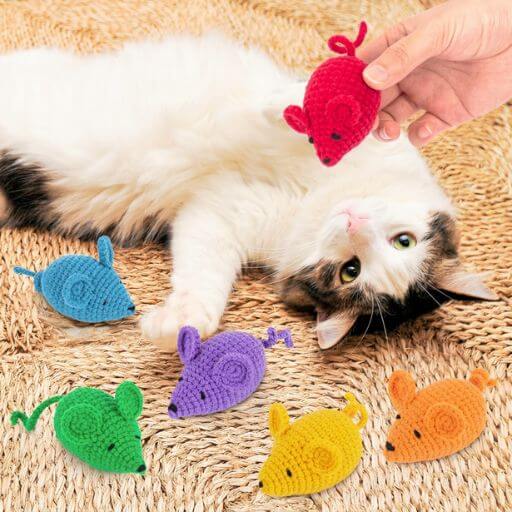 Gato deitado a brincar com ratinhos artesanais feitos de crochê em várias cores vibrantes.