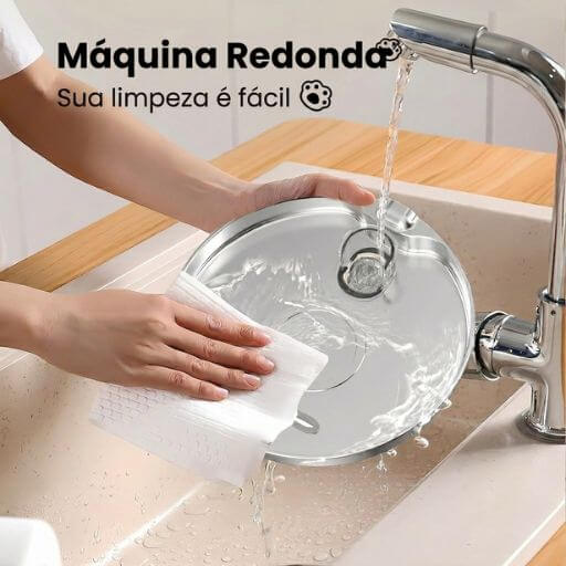 Pessoa lavando facilmente a bandeja superior de inox do bebedouro automático em água corrente na pia da cozinha.