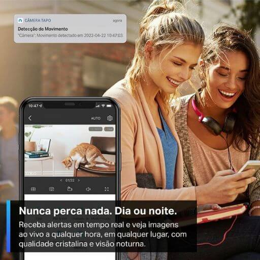 Duas mulheres sorrindo ao monitorar o gato pelo celular através de um aplicativo de notificação em tempo real.